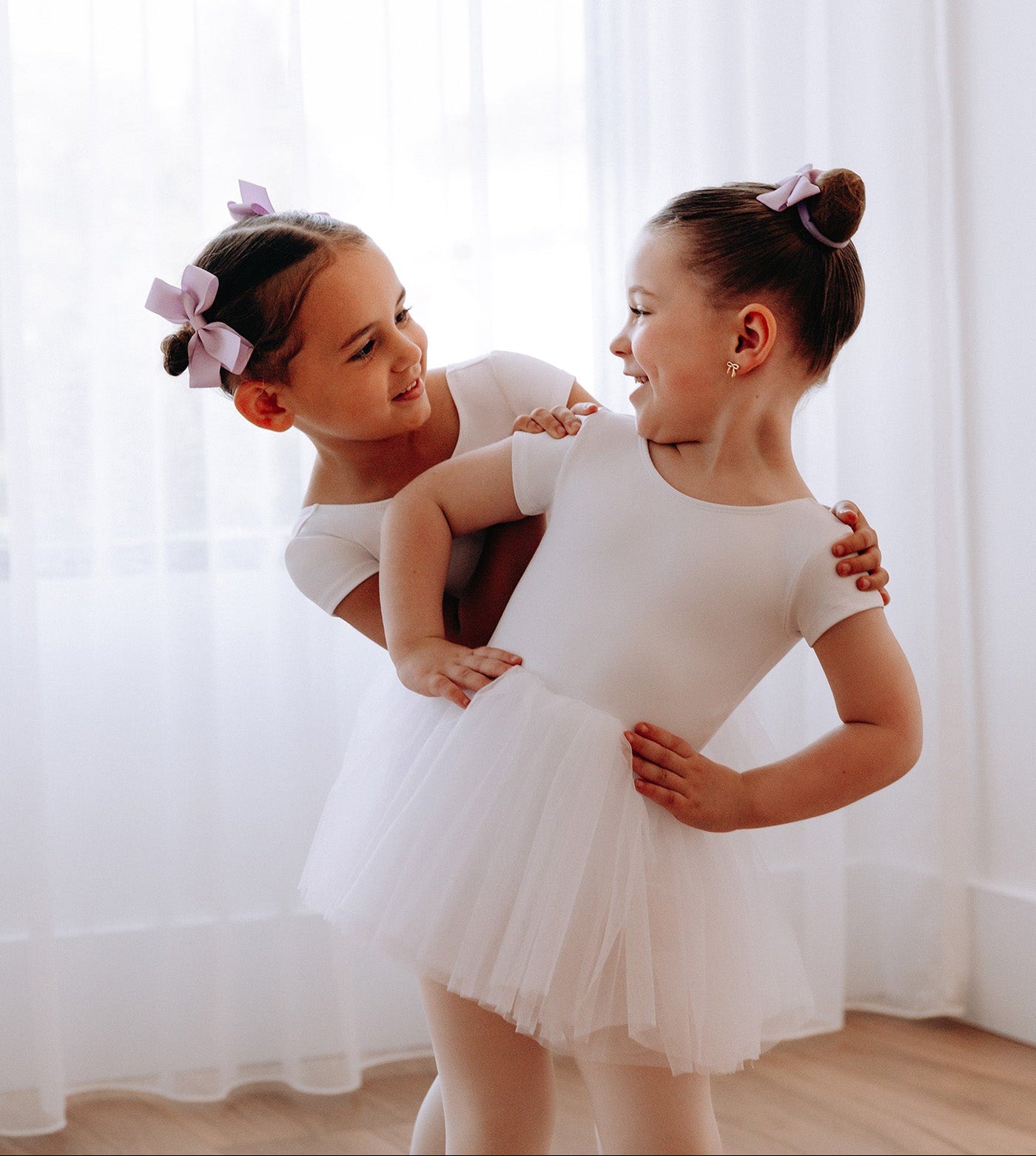 Two young girls in white ballet outfits posing against a white curtain, with 'energetiks' branding.