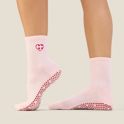 Pink grip socks with red heart and grip dots worn by a person on a beige background pilates 