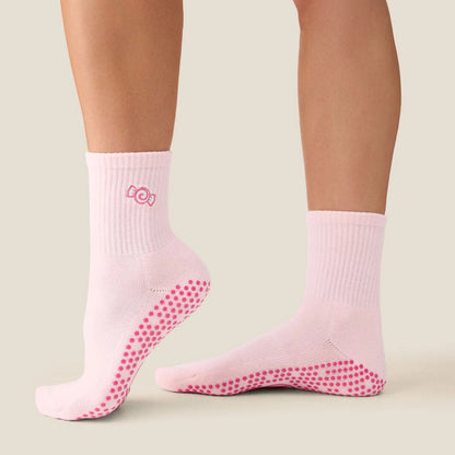 A pair of light pink ankle socks with bright pink grip dots on the sole and heel, shown on a model's feet against a light beige background.