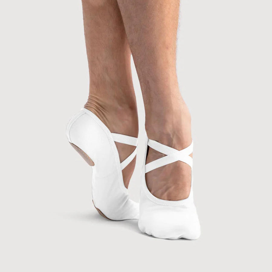 White ballet shoes with thin straps worn by a person on a light gray background