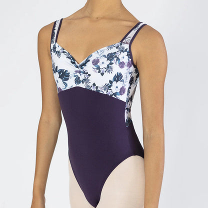 A model wearing a two-tone leotard with a dark purple solid lower half and a white floral print upper half with purple and navy botanical details.