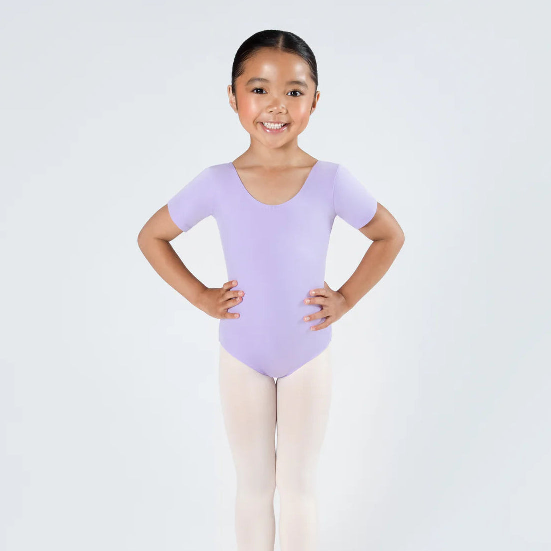 Young girl in a purple leotard and beige tights posing against a white background