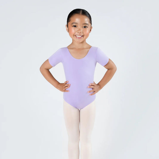 Young girl in a purple leotard and beige tights posing against a white background