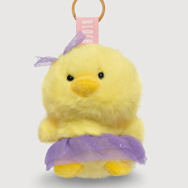 A yellow plush duck keychain charm with a purple tutu skirt and matching purple bow, attached to a gold key ring and a pink ribbon tag.