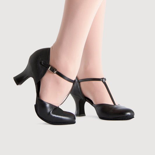 Black high-heeled shoes worn with beige stockings on a light gray background