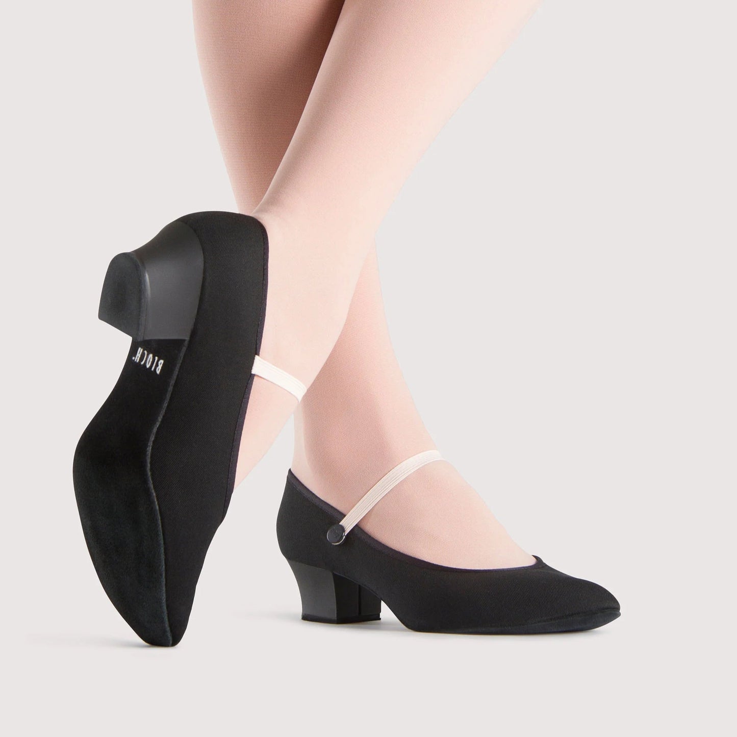 Black dance shoes worn with white tights on a light gray background