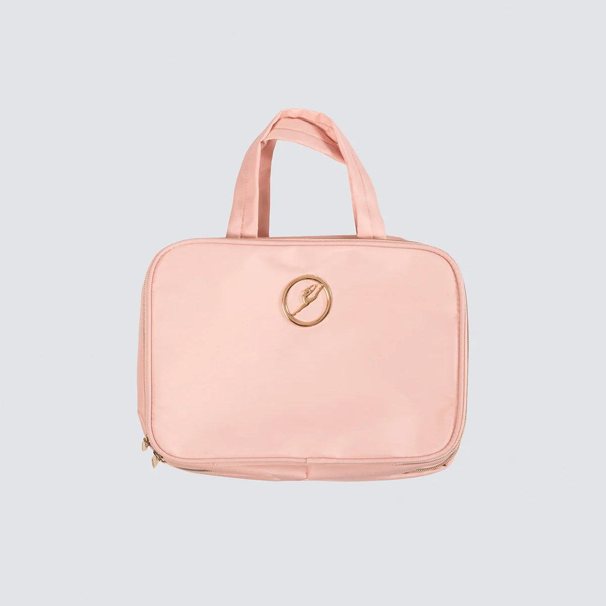 A light pink zippered toiletry bag with two top handles and a circular gold logo on the front, set against a solid light gray background.
