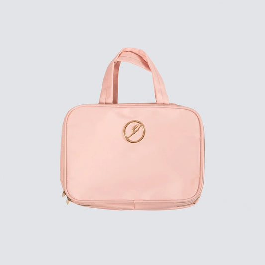 A light pink zippered toiletry bag with two top handles and a circular gold logo on the front, set against a solid light gray background.